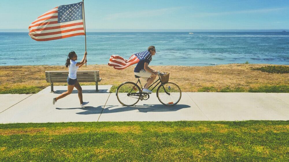 アメリカの国旗を持って走る女性と自転車に乗る男性